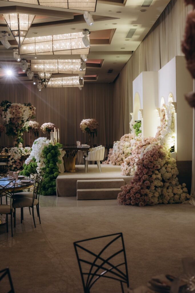 Blush and white floral cascade draping a white pedestal stage with arched niches