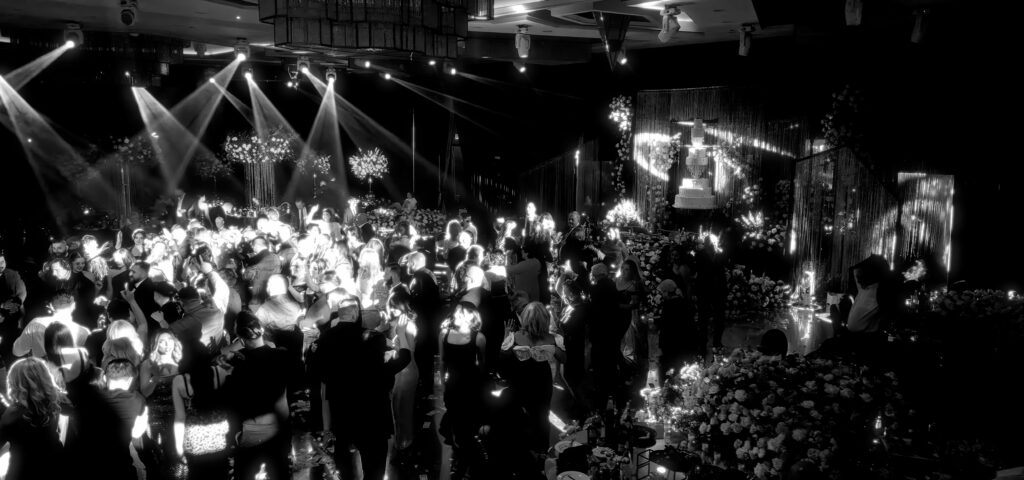 Black-and-white photo of guests dancing under sparkling lights near a floral display and cake