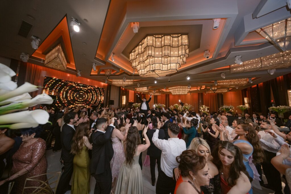 Wedding guests dancing under crystal chandeliers with orange uplighting