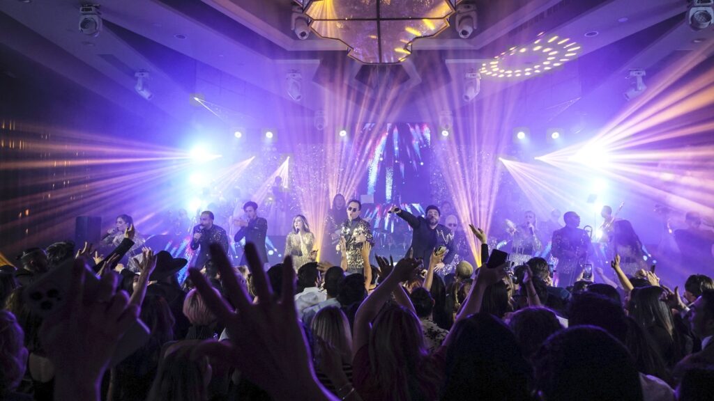 Live performers and a cheering crowd under purple and gold stage lighting