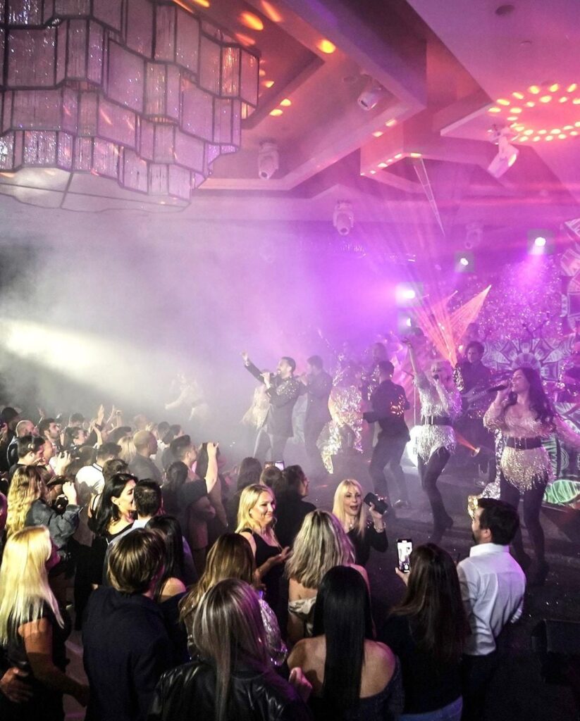 Band performing through stage smoke as guests dance under a chandelier