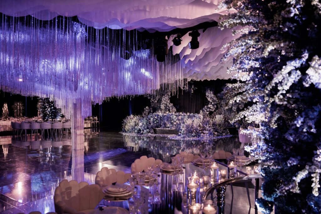 Reception hall with a blue-lit floral ceiling installation over a mirrored dance floor