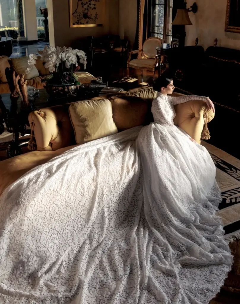 Bride in a lace wedding gown seated on a gold tufted sofa
