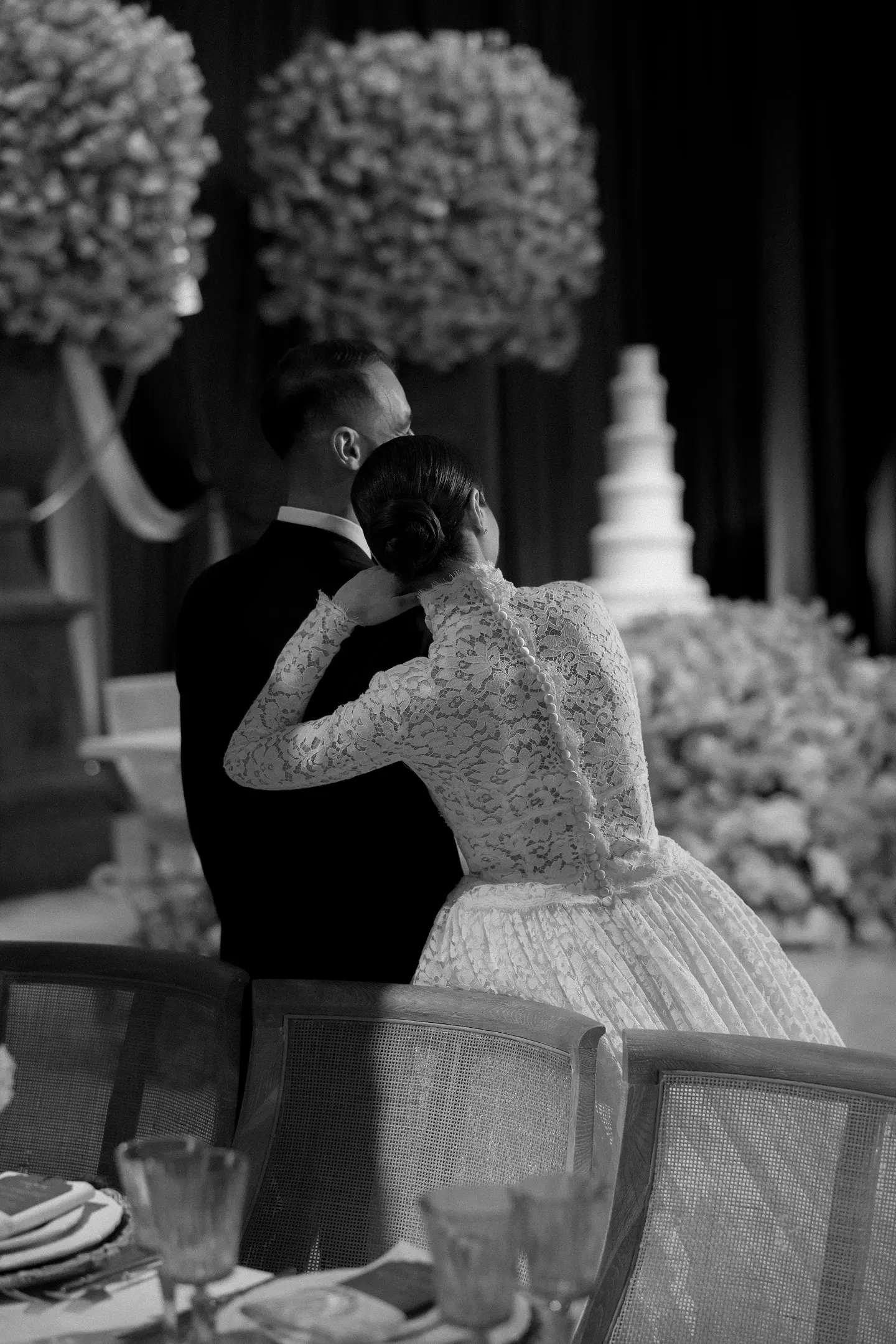 Black-and-white photo of a bride and groom embracing near a tiered wedding cake