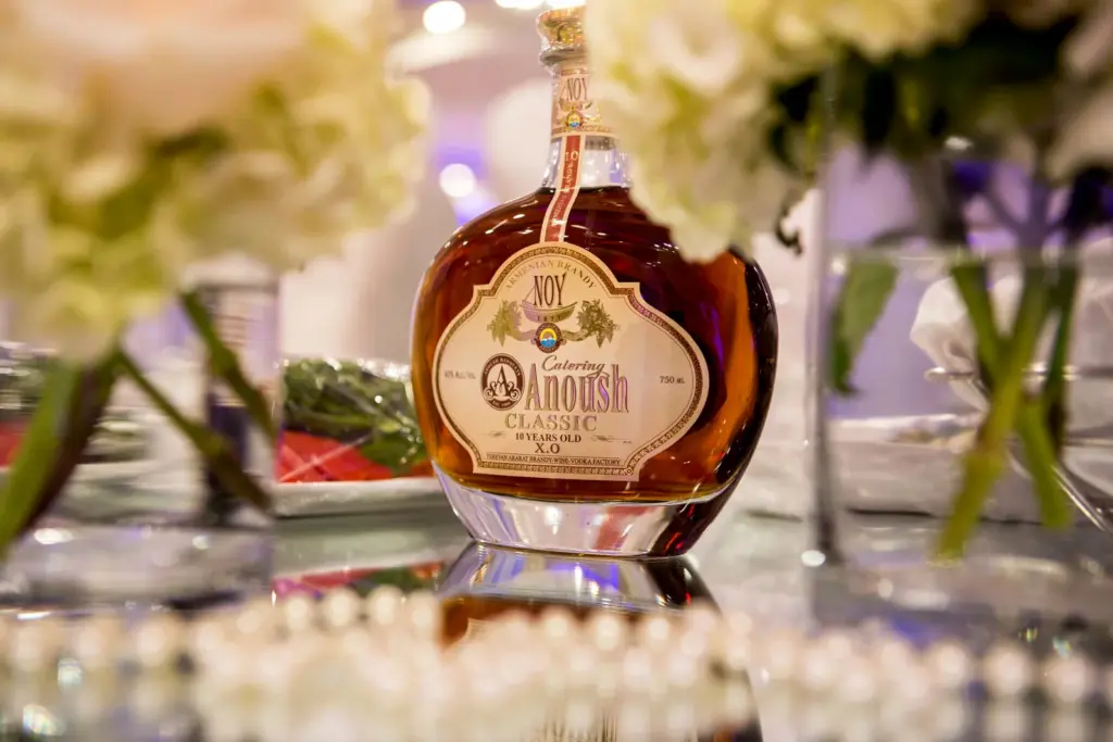 Bottle of Anoush brandy displayed among white floral centerpieces