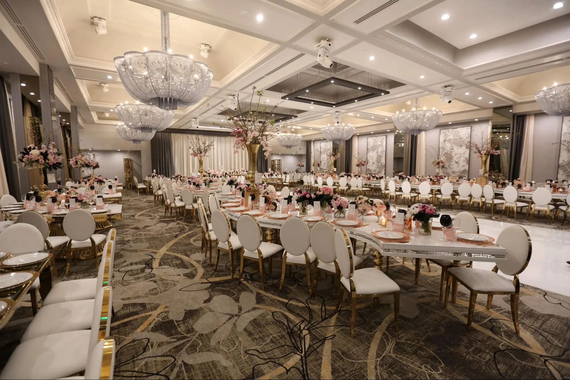 Ballroom set for a wedding reception with crystal chandeliers and floral centerpieces