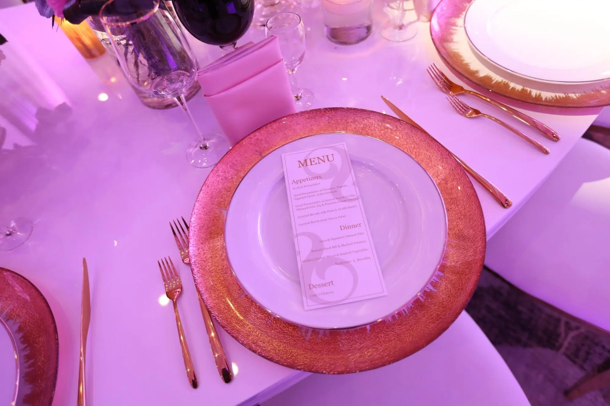 Place setting with a printed menu card, gold flatware and a pink charger plate