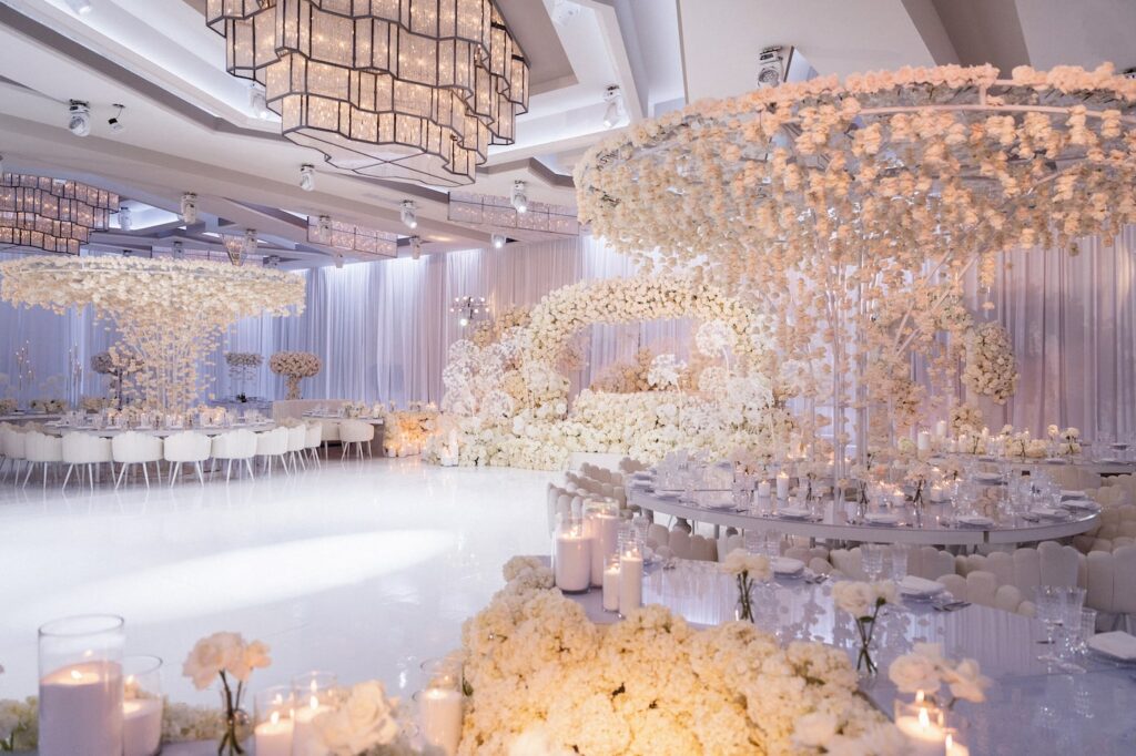 All-white reception hall with hanging floral chandeliers and a glowing dance floor
