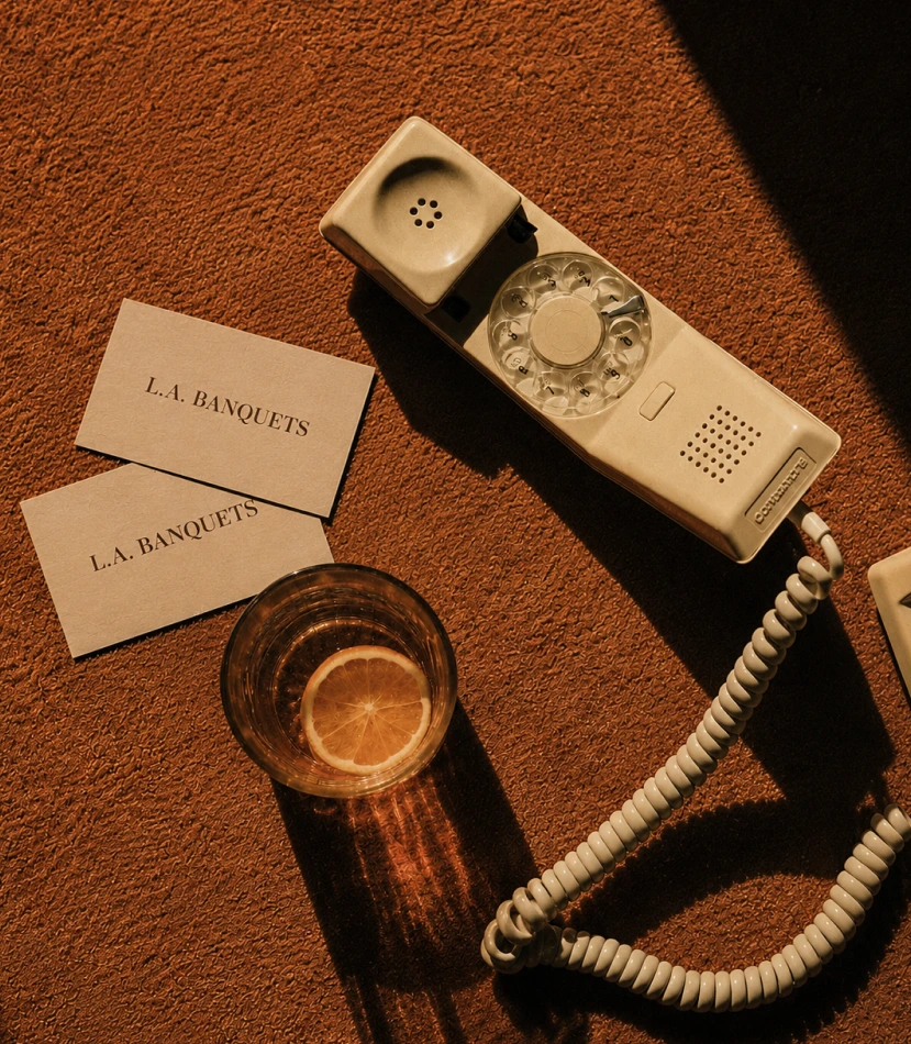 Vintage rotary phone beside L.A. Banquets business cards and a glass of lemon water
