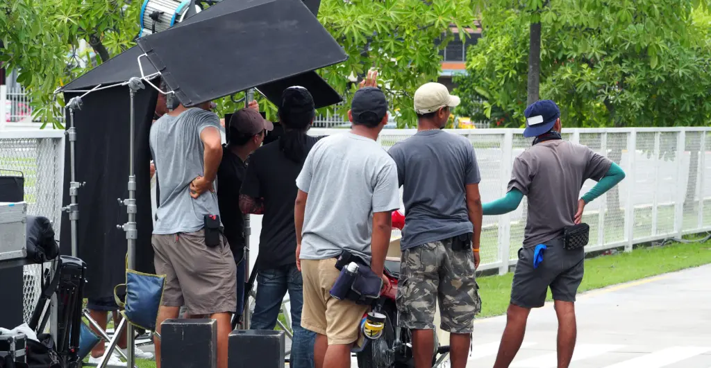 Film crew setting up lighting equipment and gear outdoors during a video shoot