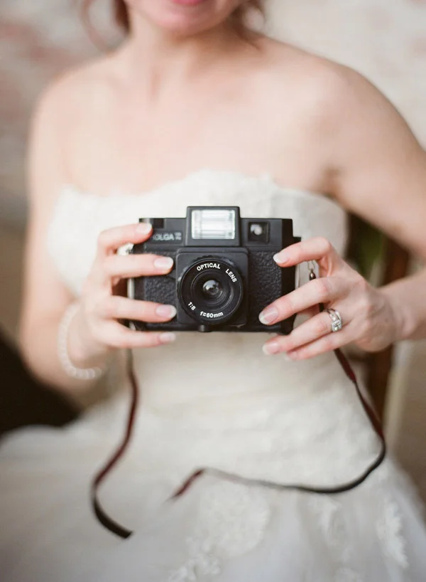 Bride holding a vintage camera, close-up on her hands and wedding gown