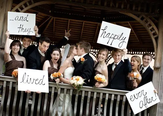 Wedding party holding signs reading and they lived happily ever after as the couple kisses