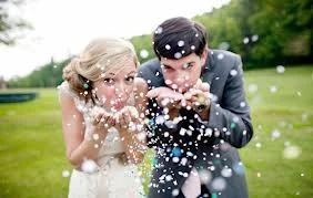 Bride and groom blowing colorful confetti into the air outdoors