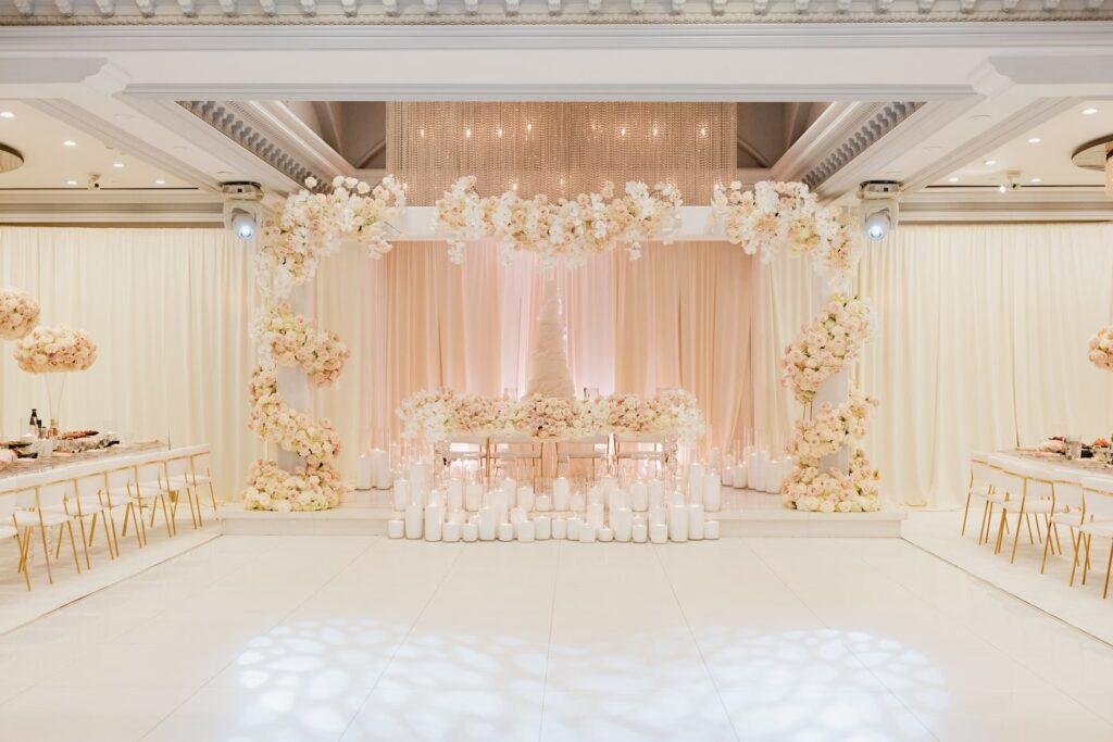 Reception hall with a floral arch backdrop and candlelit aisle leading to a sweetheart table