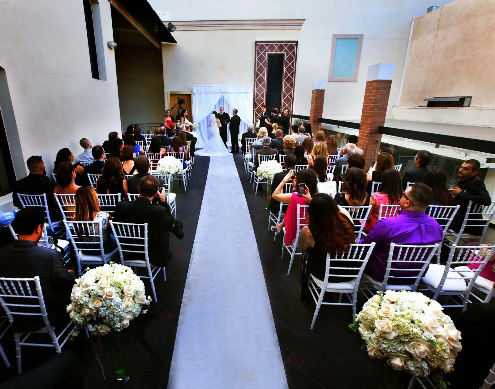Indoor wedding ceremony with a white aisle runner and floral bouquets in the foreground