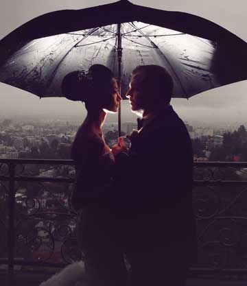 Couple silhouetted under an umbrella overlooking a city skyline at dusk