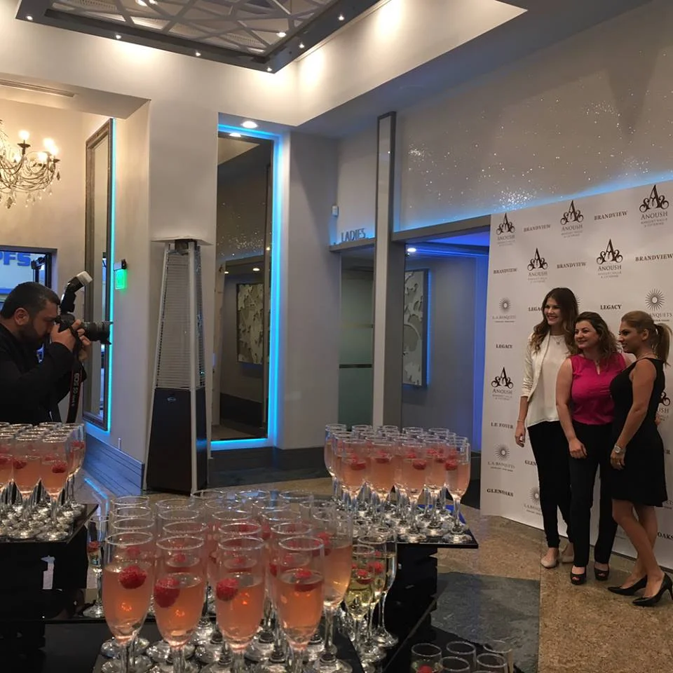 Photographer at a step-and-repeat backdrop beside trays of raspberry mocktails