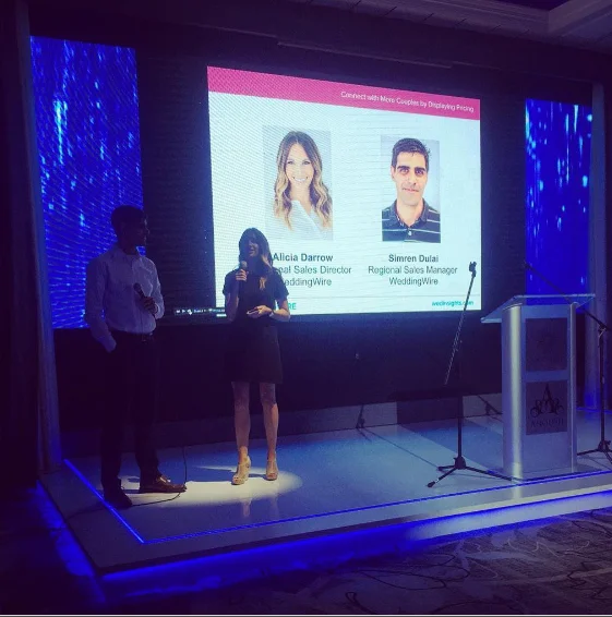 Presenters on stage beside a WeddingWire slide at an industry networking event