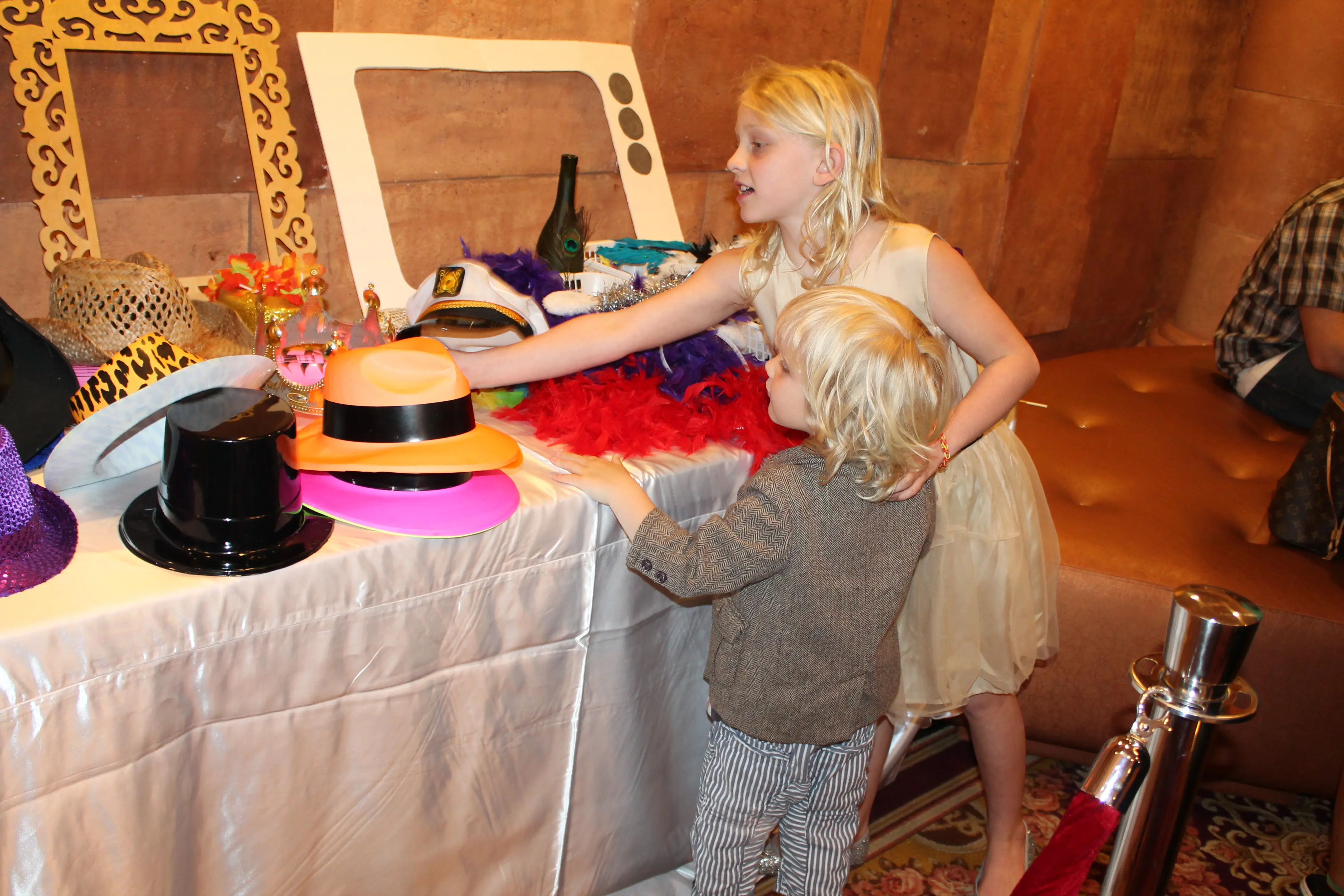 Two children choosing hats and feather boas at a photo booth prop table