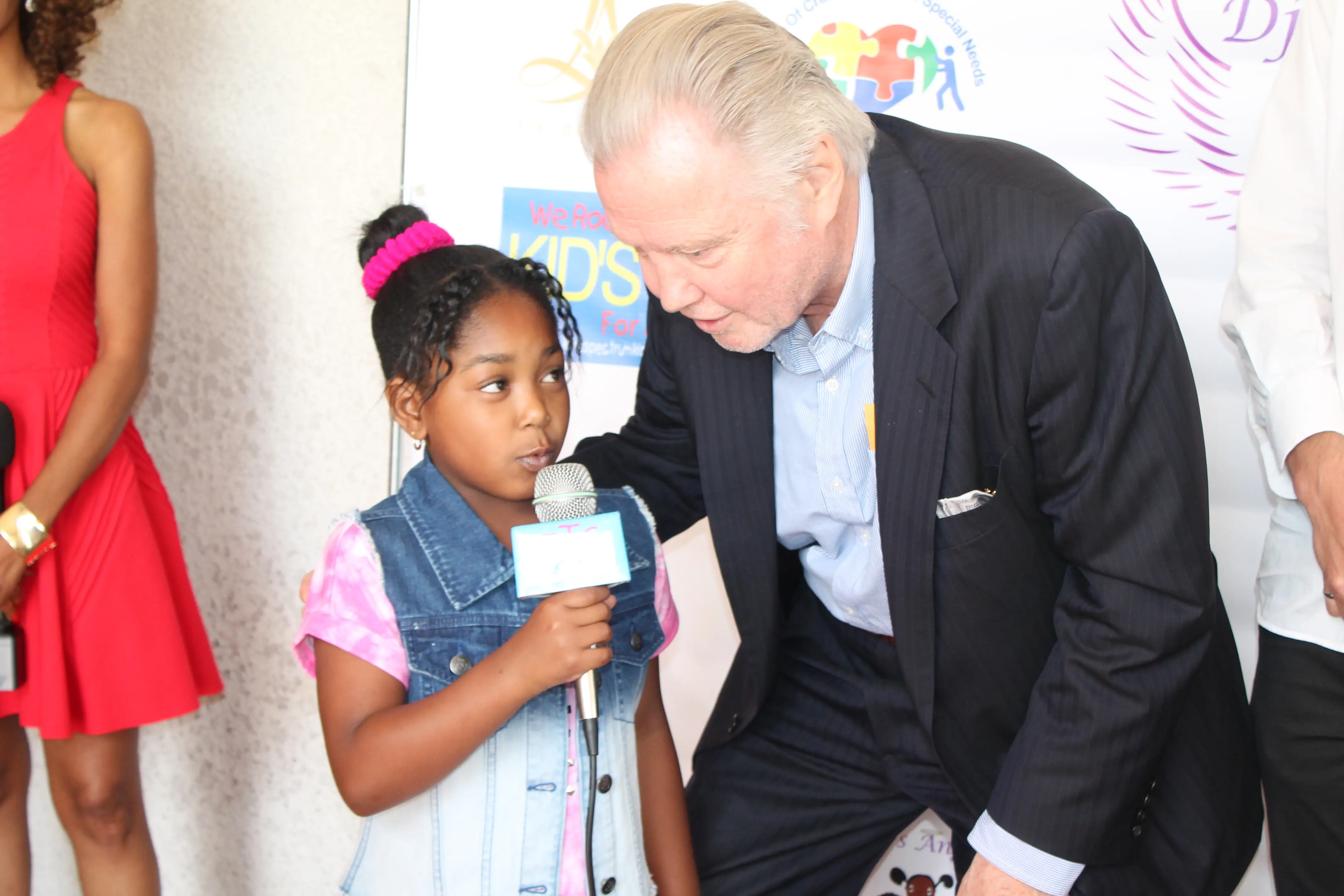 Young girl speaking into a microphone beside a guest at a charity prom event