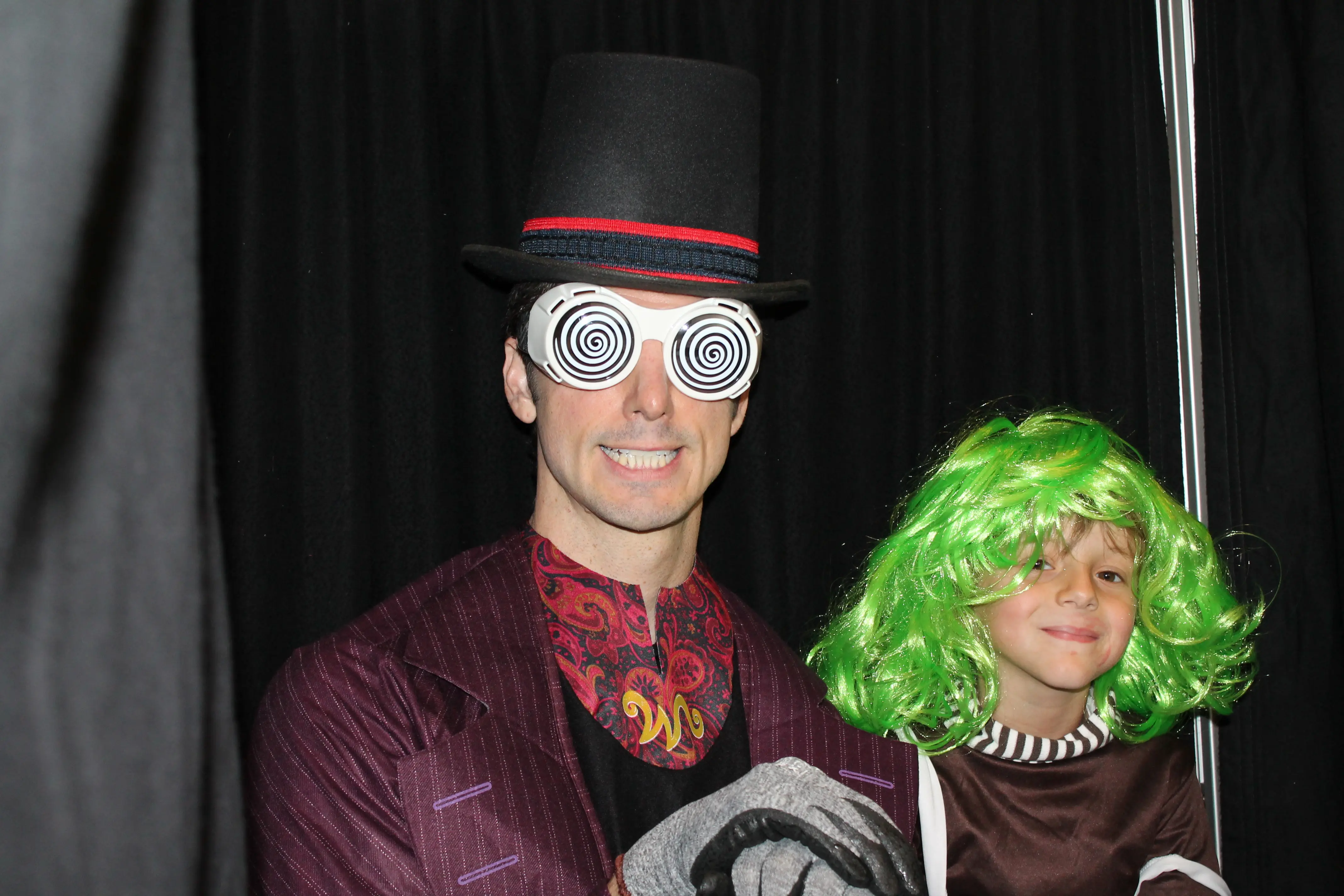 Man in a Willy Wonka costume posing with a child in a green wig at a themed prom