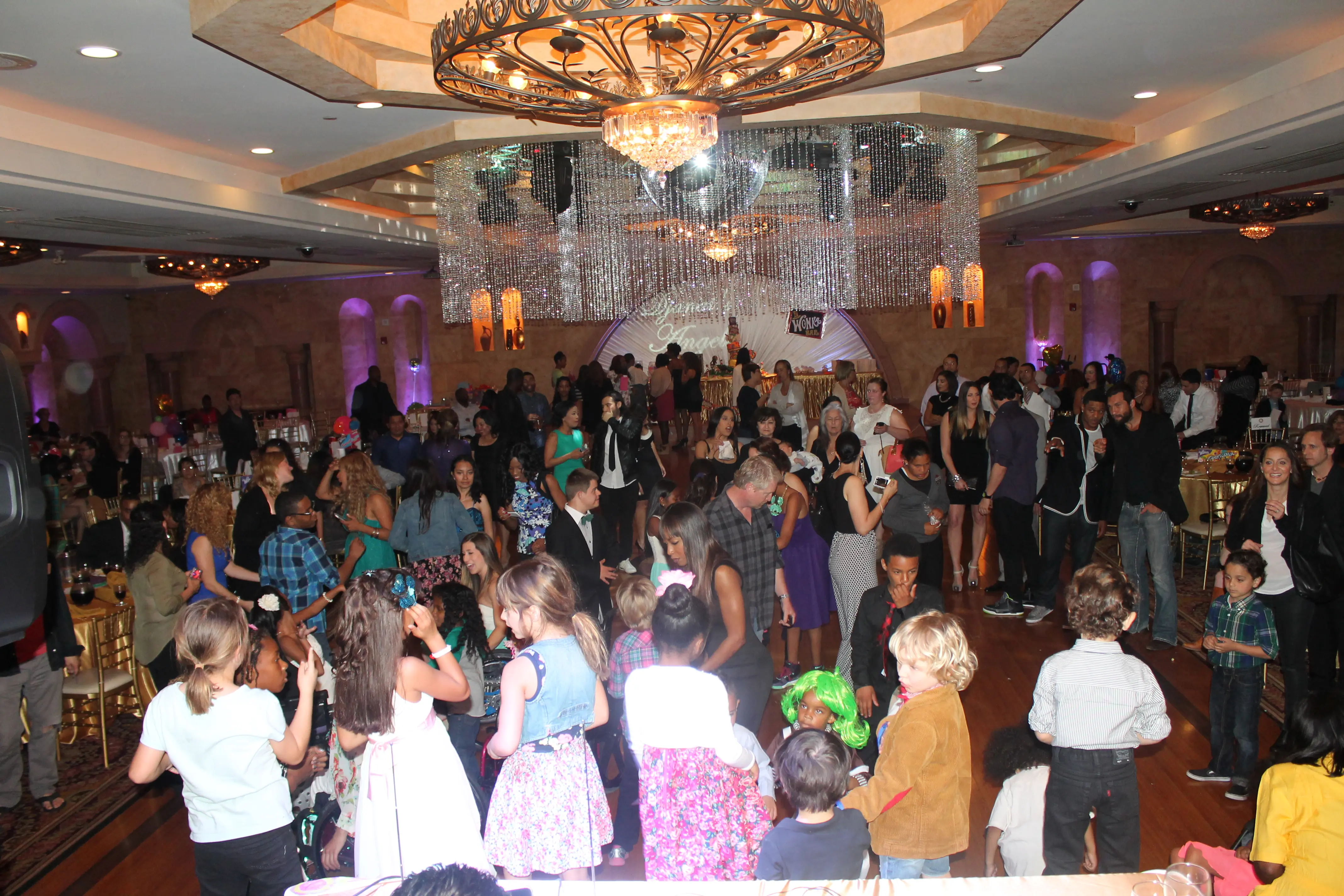 Guests dancing beneath a crystal chandelier in a ballroom during a themed prom