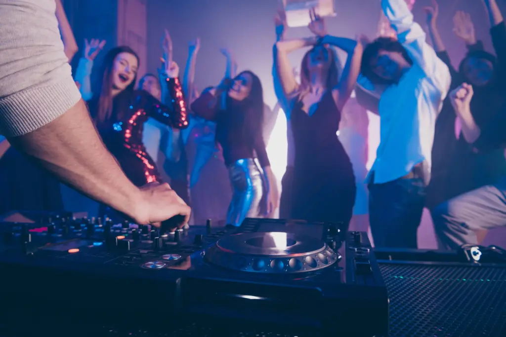 DJ mixing music on a turntable as guests dance under colorful party lights