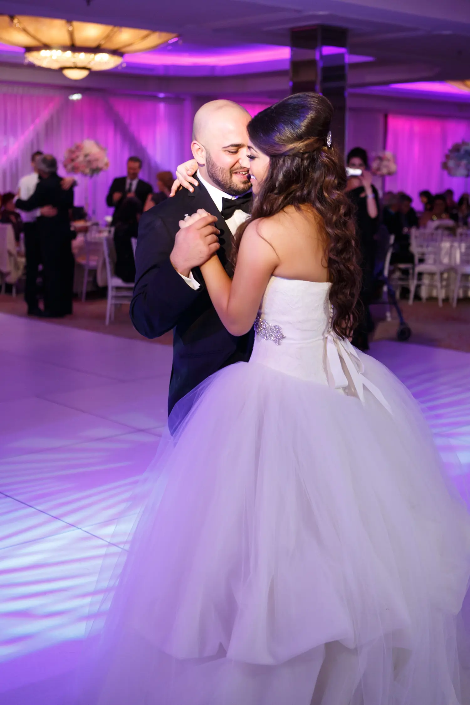 Bride and groom dancing together on a dance floor lit with purple uplighting