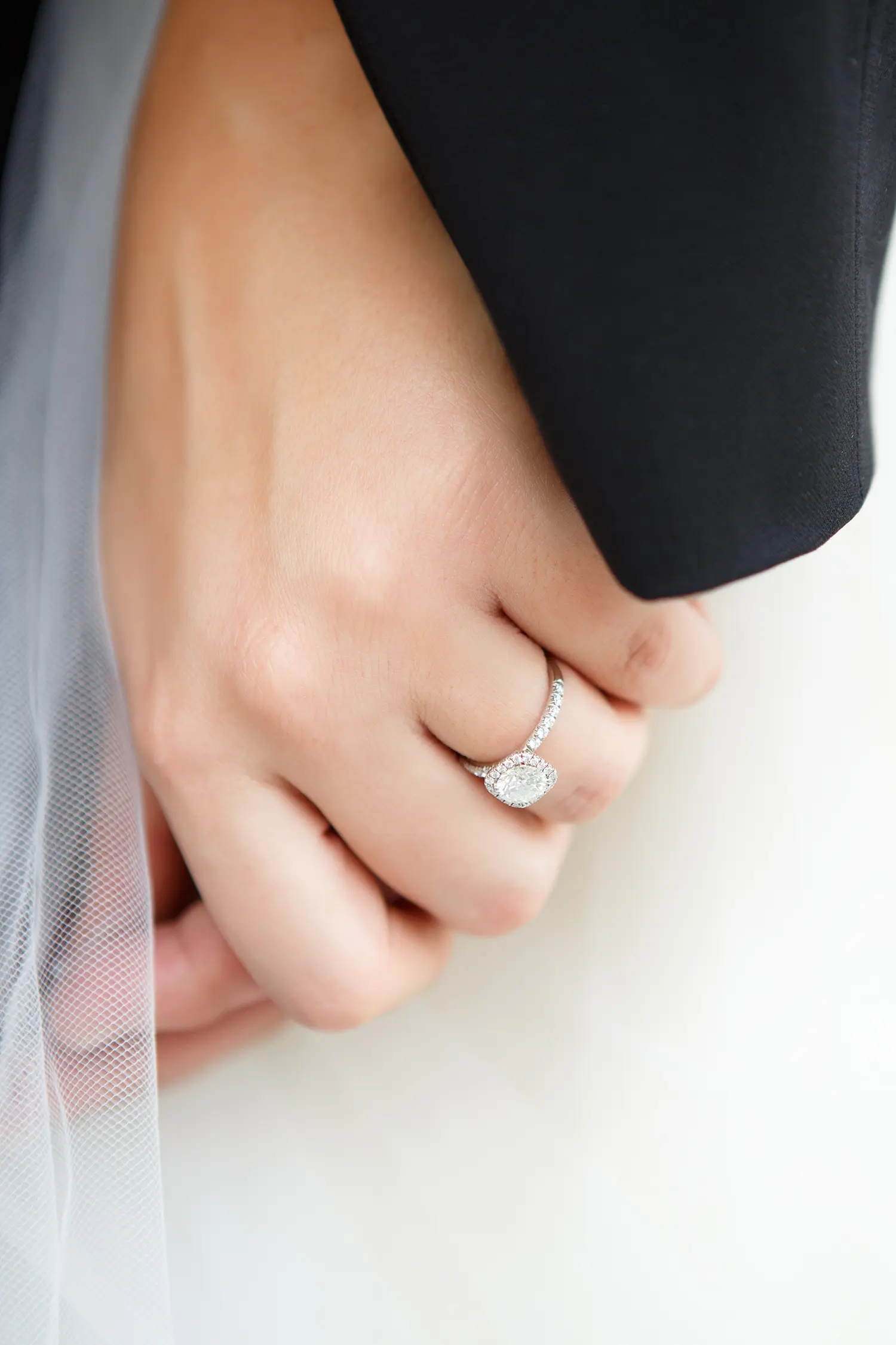 Close-up of a bride's hand wearing an engagement ring resting on the groom's arm