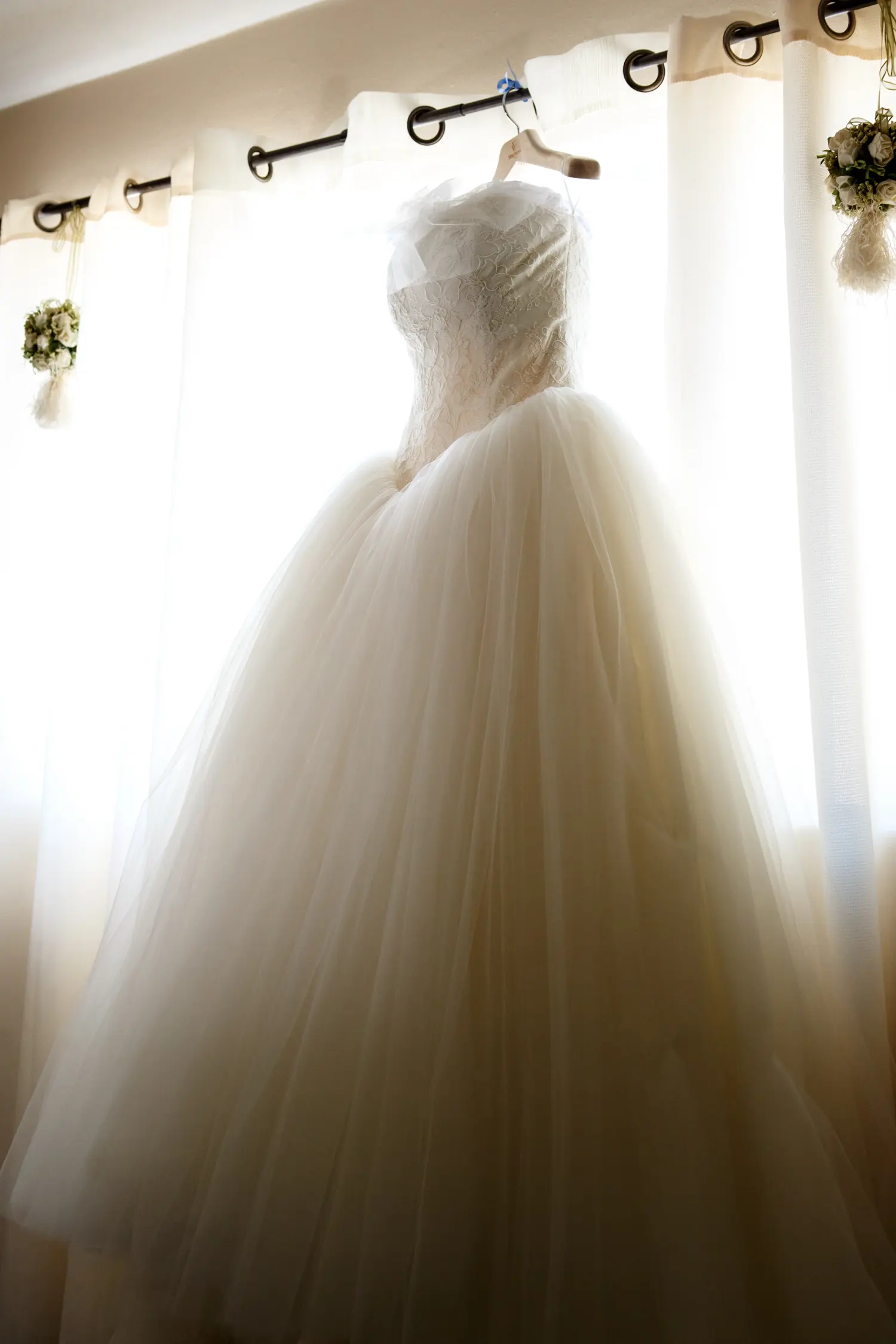 Wedding dress hanging in a sunlit window before the ceremony