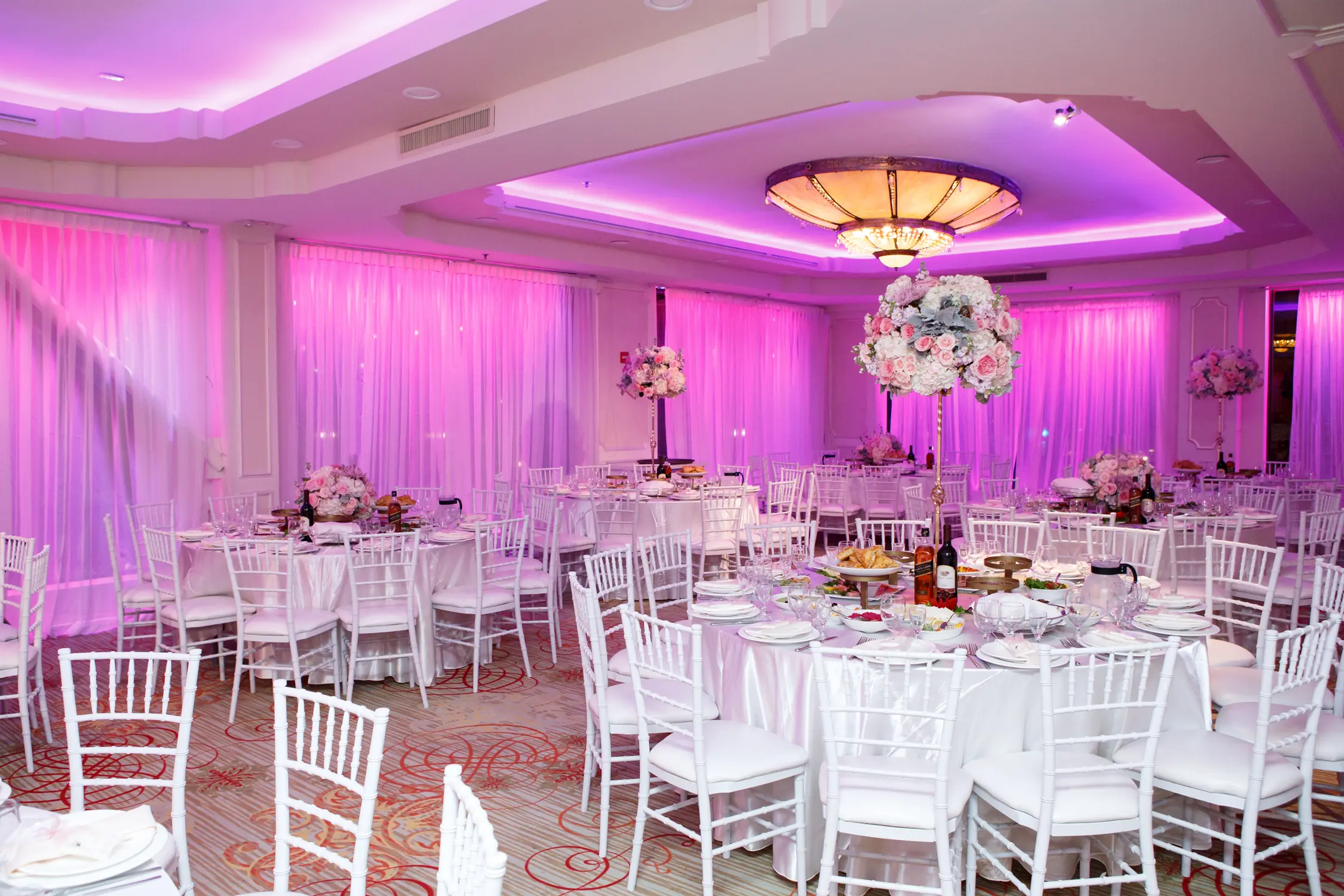 Reception ballroom set with round tables and pink uplighting