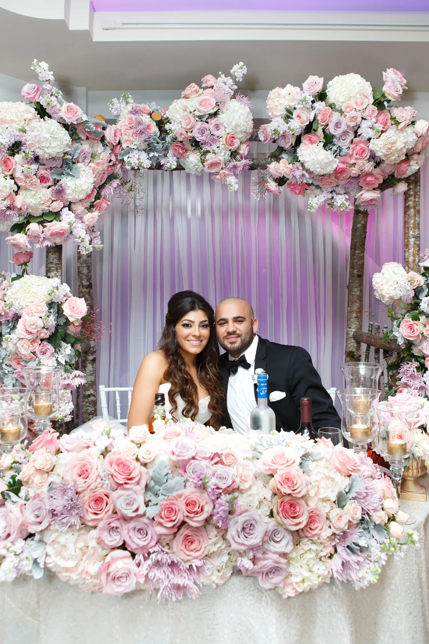 Bride and groom smiling at their flower-framed sweetheart table