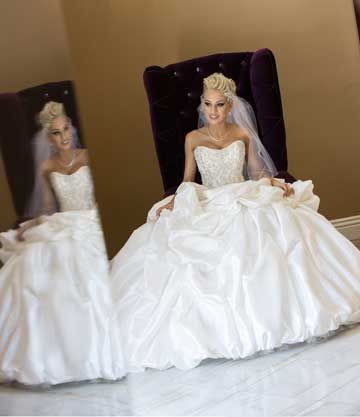 Bride in a ball gown seated in a velvet chair with mirror reflection