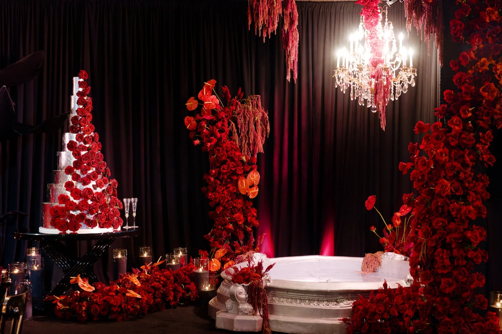 Dramatic red floral installation with a tiered cake and chandelier in a dark ballroom