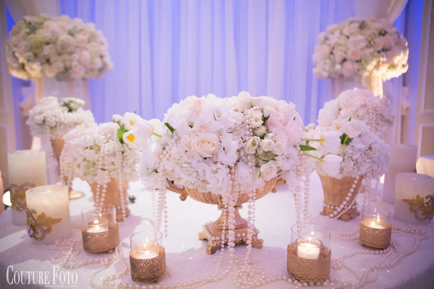 White floral centerpiece with pearl strands and candles on a reception table