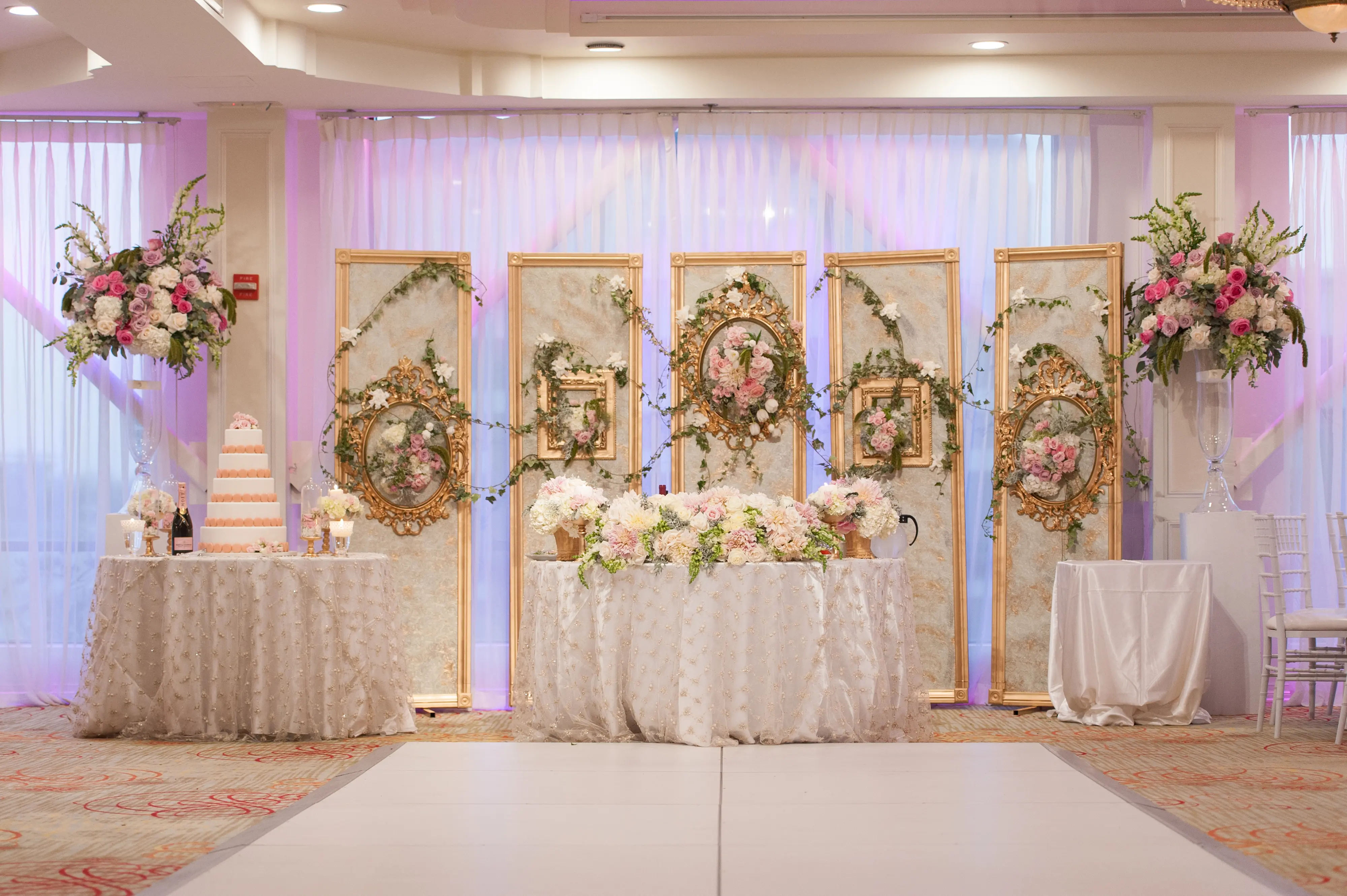 Sweetheart table backdrop with gold frames, greenery and pink floral arrangements