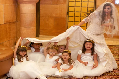 Bride laughing with flower girls playing under her wedding veil