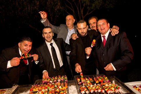 Men in suits enjoying grilled skewers at an evening barbecue