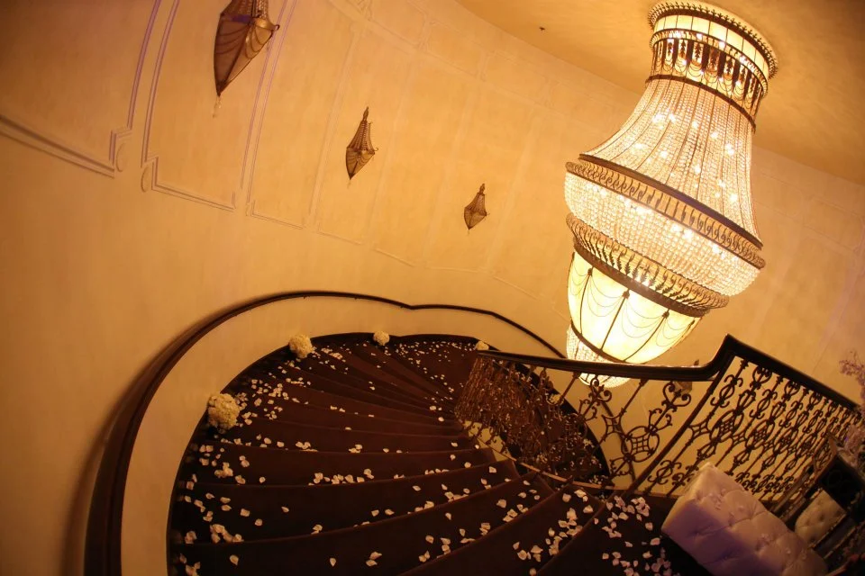 Rose petals scattered on a curved staircase beneath a crystal chandelier
