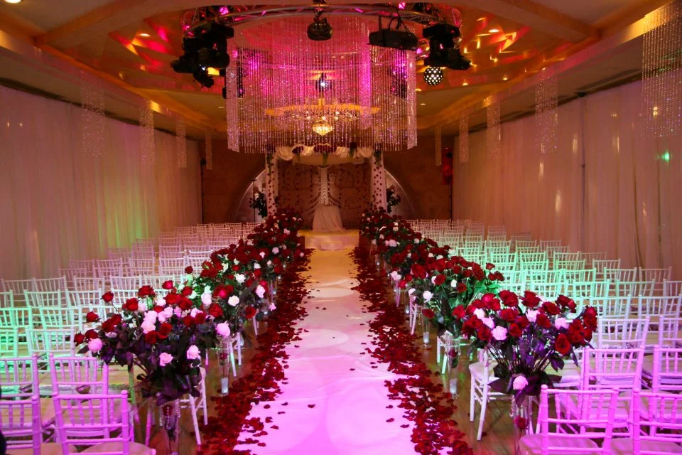 Ceremony aisle lined with red and white rose arrangements under colorful lighting
