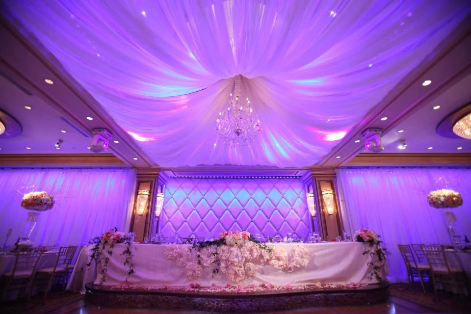 Ballroom with purple uplighting, draped ceiling and a floral sweetheart table
