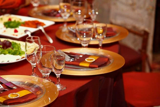Banquet table set with gold-rimmed plates, wine glasses and burgundy linens