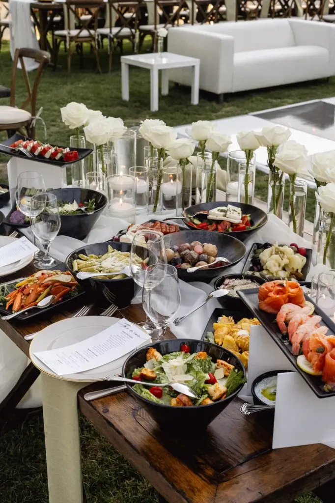Outdoor reception food display with salads, seafood, and a tall white orchid arrangement