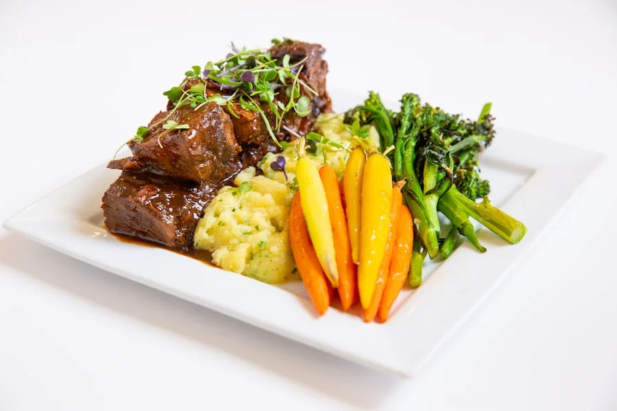 Braised short rib plated with mashed potatoes, carrots, and broccolini