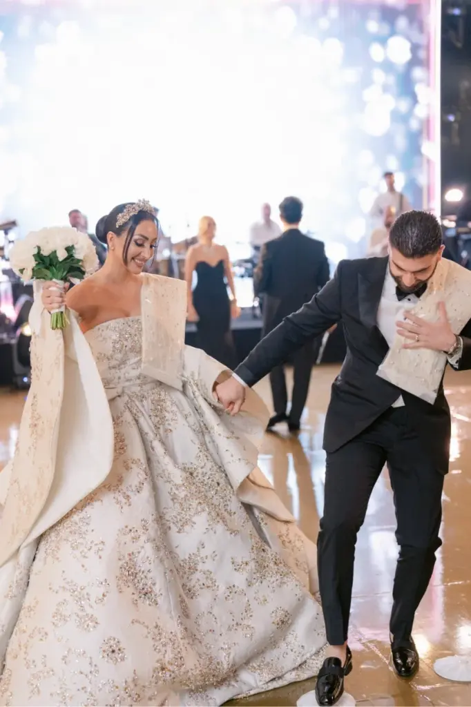 Bride and groom walking hand in hand holding a bouquet across the dance floor