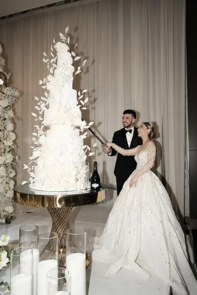 Bride and groom cutting a tall white floral wedding cake with a sword