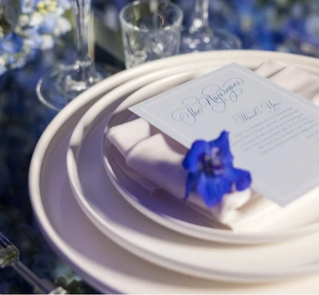 Place setting with a blue floral accent and a personalized name card on a white plate