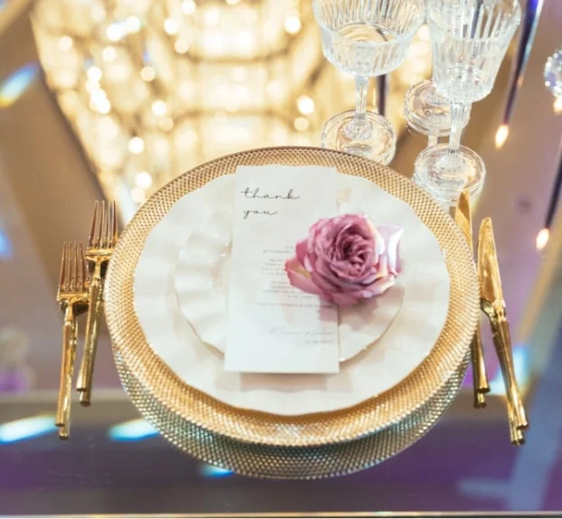 Gold charger plate setting with a "thank you" card and pink rose beside gold flatware
