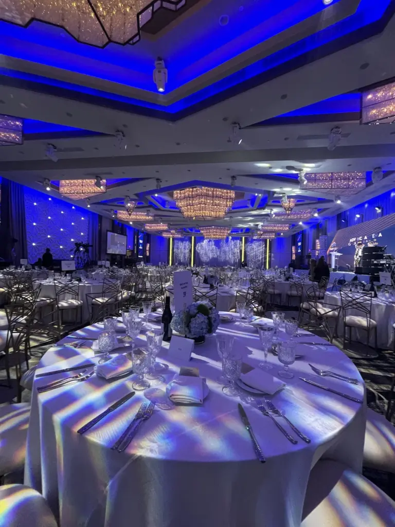Ballroom gala setup with round tables, floral centerpieces, and blue stage lighting