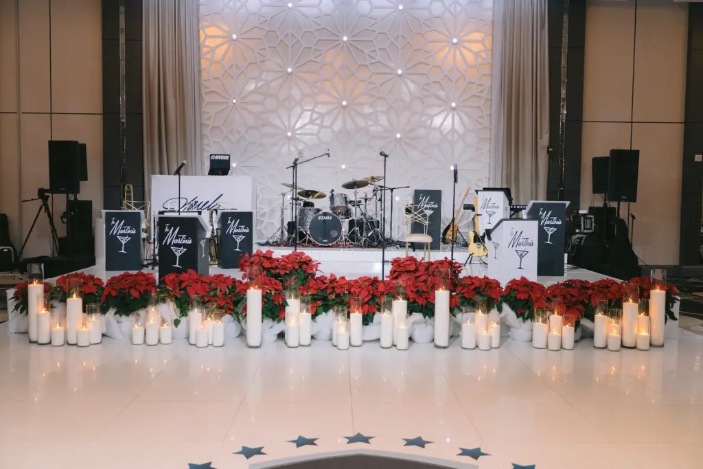 Ballroom stage with drum kit and band setup framed by poinsettias and candles for a holiday gala